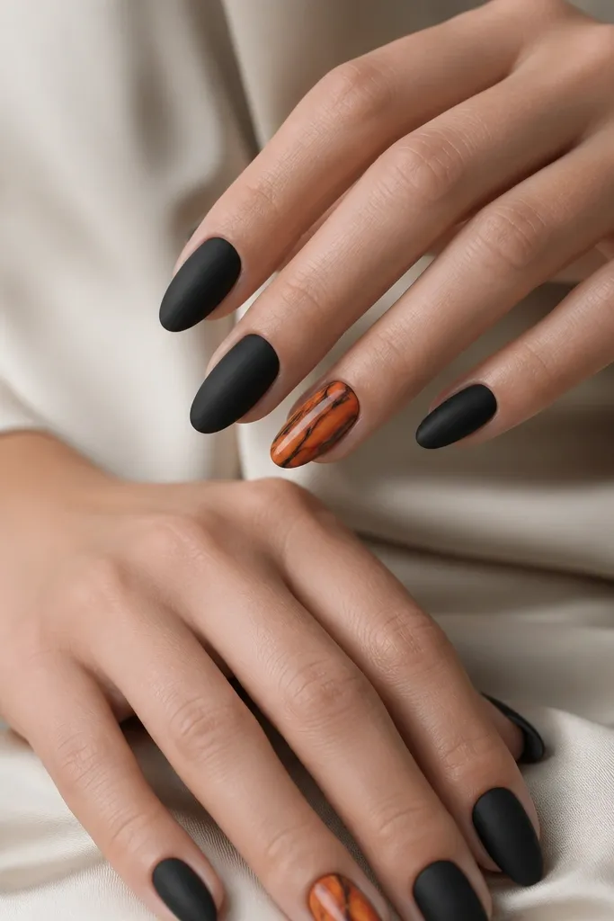 Mostly matte black nails. One accent nail per hand has an orange marble pattern: swirling orange and amber on a semi-gloss base with thin black veins running through it. The marble sits in the center like a panel.