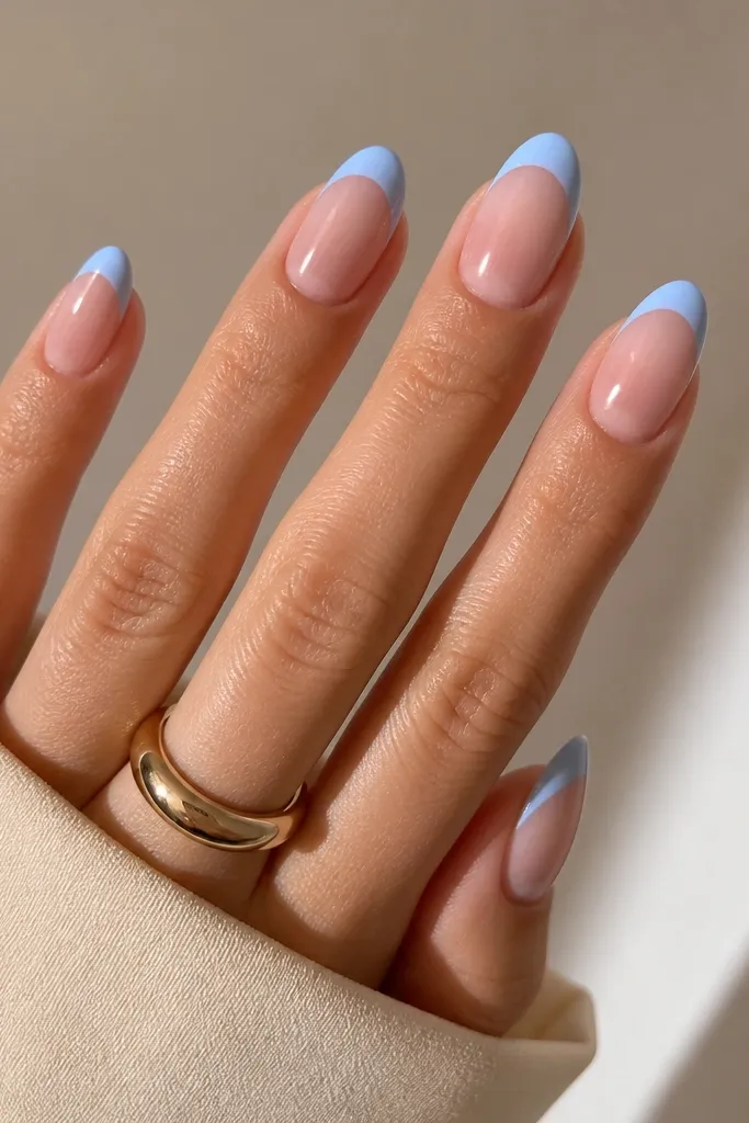 Medium almond nails with nude-pink base. The French tips are painted a clean sky blue arc. The cuticle area is left bare and glossy, creating a crisp negative-space border.