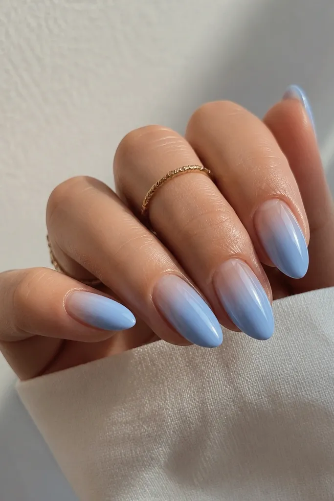 Medium almond nails with sky blue that fades upward into a clear, jelly-like cuticle zone. The gradient is smooth and looks like a watercolor wash.