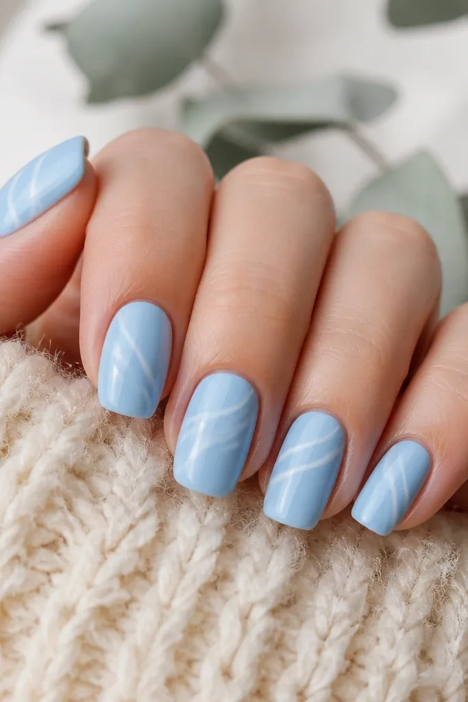 Short coffin nails in solid sky blue. Each nail has one or two thin white curved lines running diagonally, like wave crests. Glossy topcoat makes the lines pop.