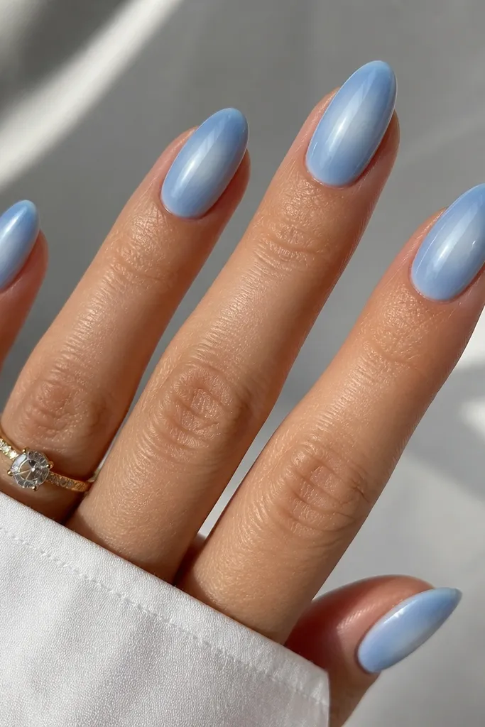 Medium almond nails with a sky blue aura effect. The center looks bright and surrounded by a soft, cloudy halo fading outward. The cuticle is slightly lighter than the sides.
