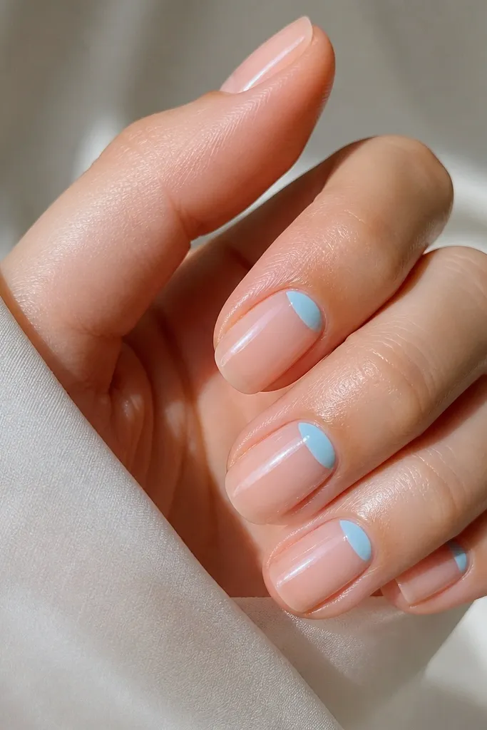 Natural nude-clear nails with baby sky blue half-moon shapes at the cuticles. The half-moons are crisp and glossy, leaving the rest of the nail sheer.
