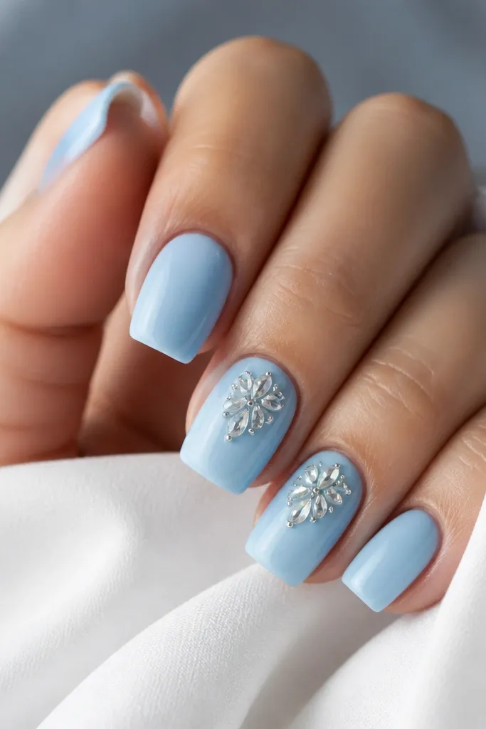 Most nails are solid sky blue. Two accent nails have a cluster of small teardrop rhinestones near the center and toward the cuticle, with a glossy finish.