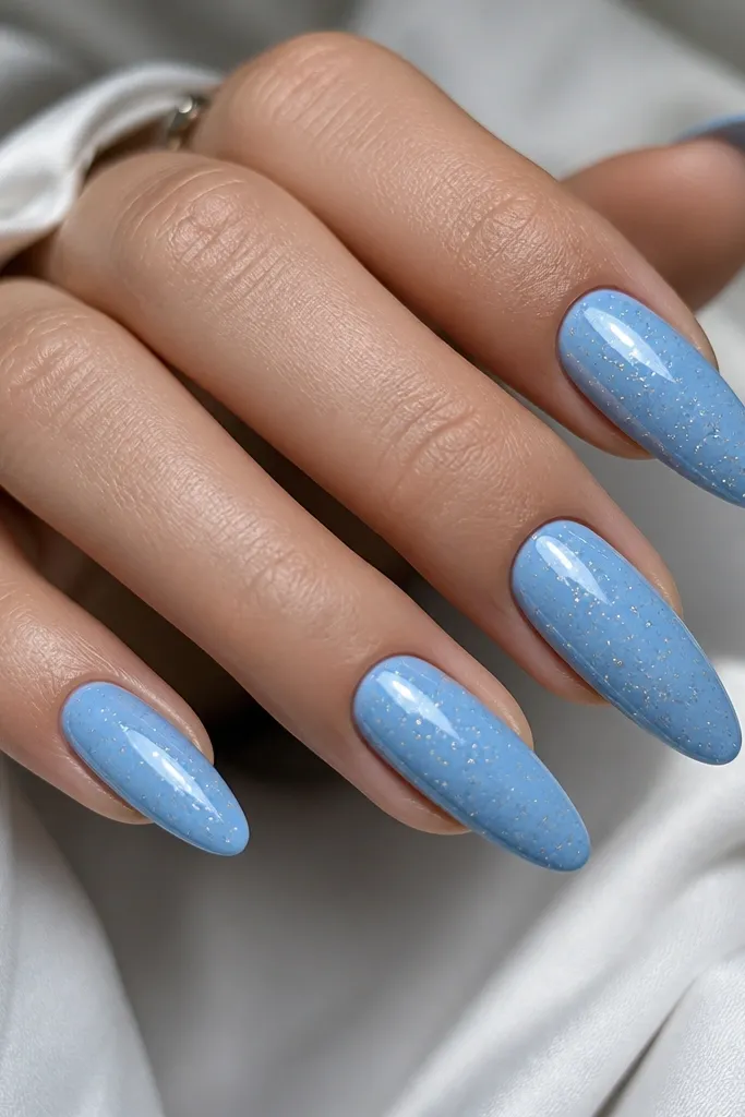 Long almond nails in sky blue. The surface has scattered tiny silver dot specks like stars, with a glossy finish that makes the dots sparkle.