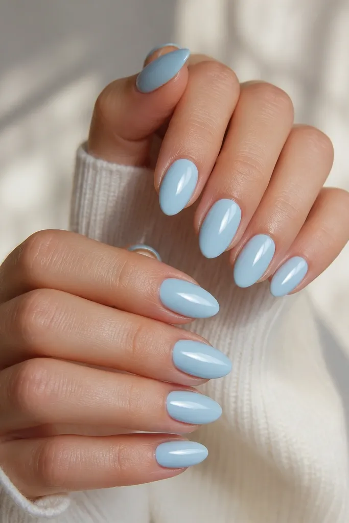Hands with medium almond nails painted a milky sky blue, all ten nails glossy and smooth with no art. The light reflects as a clean mirror highlight along each nail.