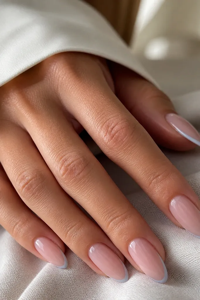 Almond nails with nude-pink base. Only a very thin baby-blue line sits at the tip edge, almost like a micro French. The rest is clean nude with high gloss.