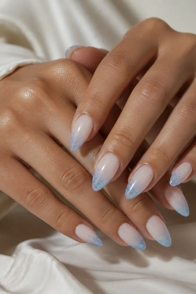 Almond nails with a sheer milky base. The tips fade from clear to sky-blue glitter, densest at the very edge and lightening toward the middle.