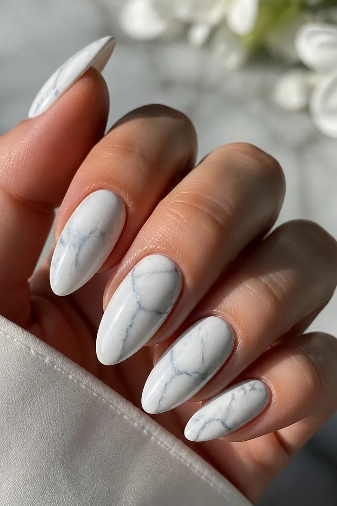 Almond nails with a white marble base. Thin sky-blue veins run through like natural stone, with glossy finish and soft gray shading around the veins.