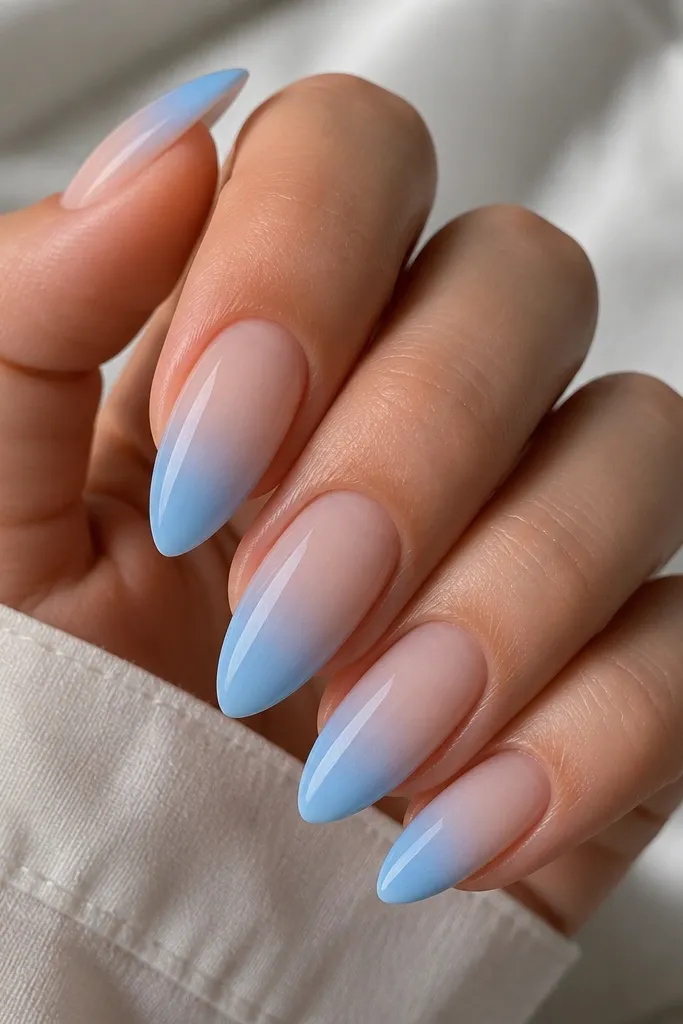 Almond nails with a smooth sky-blue ombre that starts deep at the tip and fades into a milky nude near the cuticle. The gradient is soft with no hard lines.