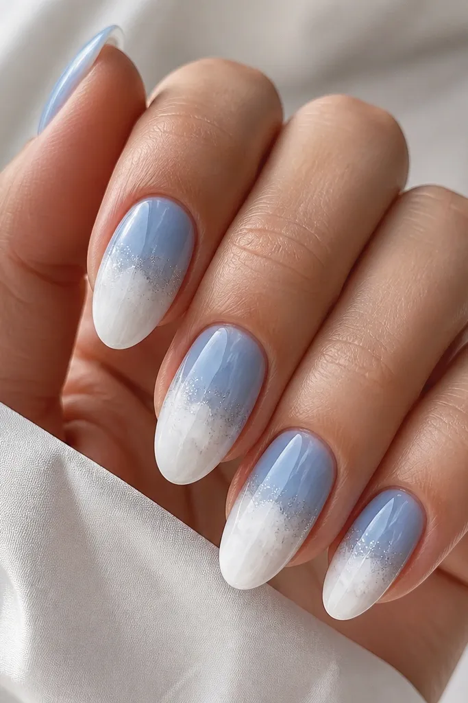 Medium almond nails with a soft white cloud effect at the tips, sky blue base fading into the cloud, and a fine silver micro-glitter sprinkled only around the cloud edge. Glossy finish throughout.