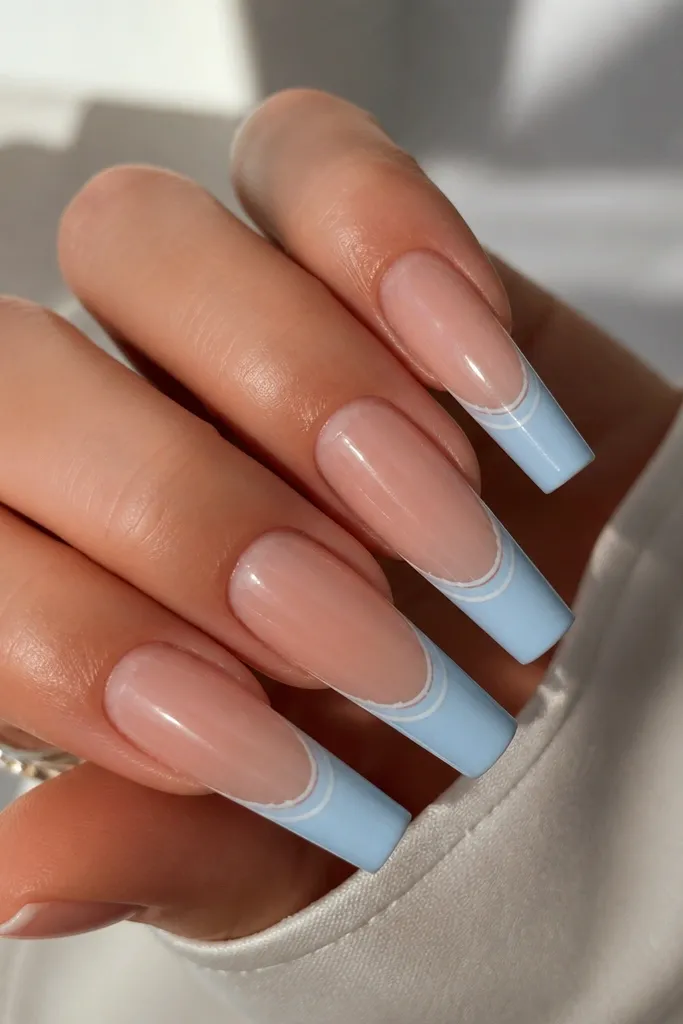Long coffin nails with sky blue French tips that are crisp and even, plus two hairline white stripes running parallel inside the blue area. The rest of the nail is sheer nude with glossy finish.