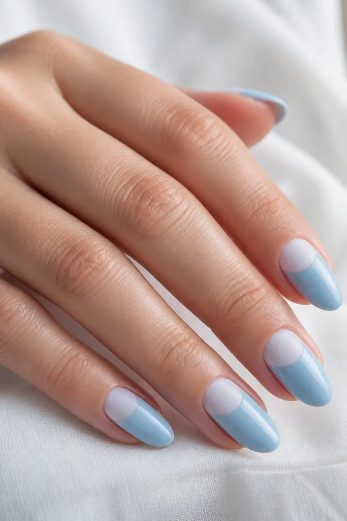 Medium almond nails with frosted white at the cuticle half-moon and sky blue at the tips. The frosted area looks slightly matte and powdery; the rest is glossy. Clean, sharp edges between colors.