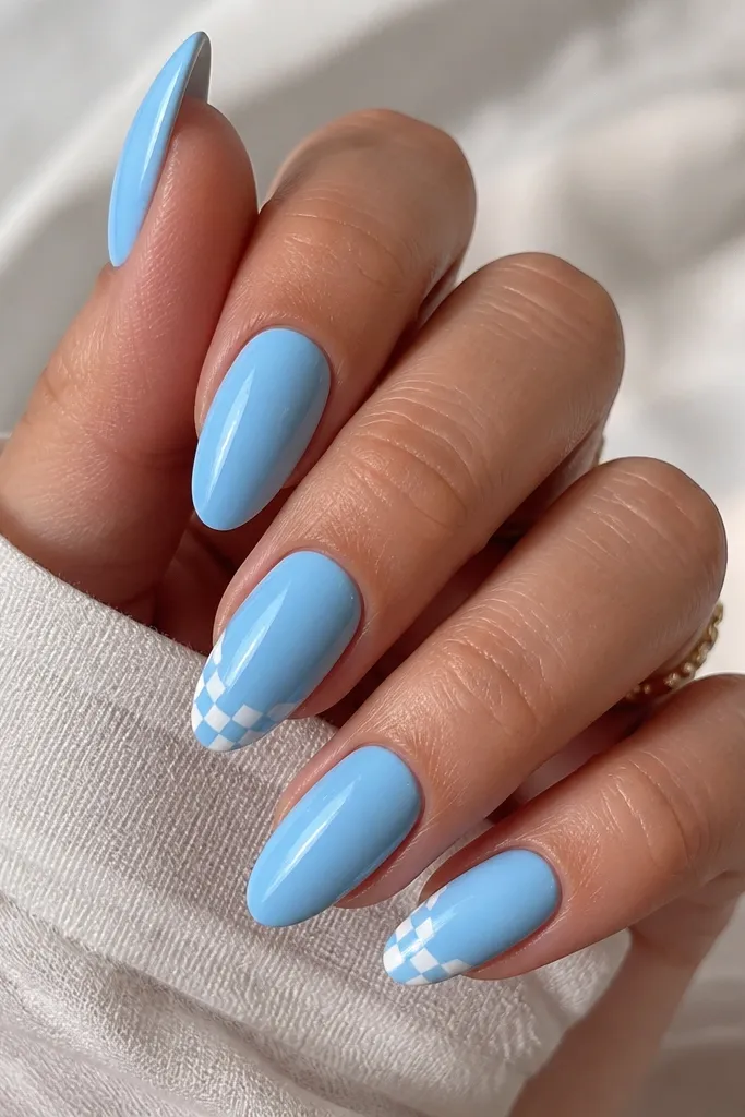 Almond nails where most nails are solid sky blue. One or two nails show a small checkerboard made of sky blue and white squares near the tip. Glossy finish on all nails.