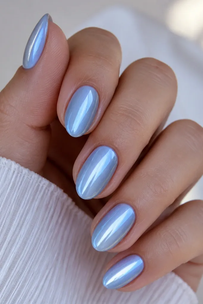 Set of short almond nails painted icy sky blue with a single bright cat eye stripe running straight down the center; high-gloss top coat reflects light like glass.