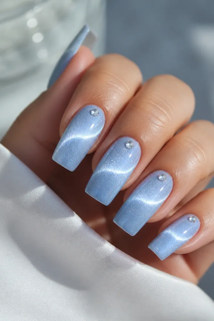Long square nails in soft powder blue with a curved magnetic arc that looks like a halo across the middle; tiny clear crystal sits near the cuticle.