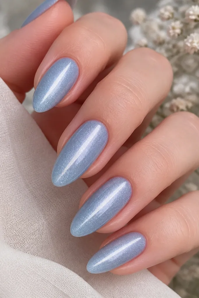 Almond nails in misty sky blue with fine silver micro-glitter scattered lightly; cat eye stripe is bright and crisp, centered.