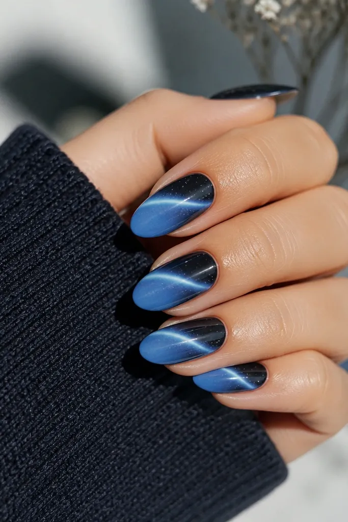 Mid-length almond nails with deep navy at the base fading into sky blue; a bright cat eye stripe; tiny white specks like stars scattered near the cuticle.