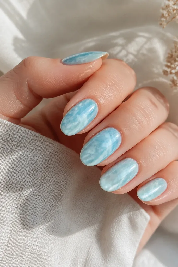 Medium oval nails with sky blue marble swirls in white and light teal; a bright cat eye stripe runs through the center like a vein.