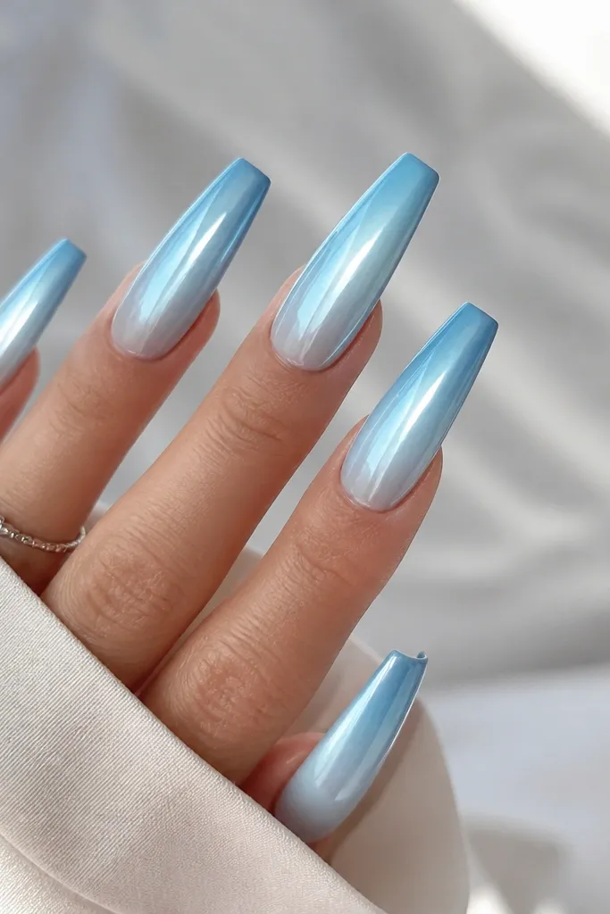 Long coffin nails with a gradient from pale sky blue at the cuticle to deeper sky blue at the tips. The entire nail is chrome mirror finish, and the ombré transitions smoothly without hard lines.
