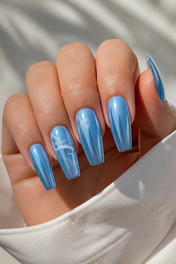 Medium coffin nails with sky blue mirror chrome. Thin white cloud-like lines curve across two nails, like wispy strokes, while other nails stay full chrome. Glossy shine remains uniform.