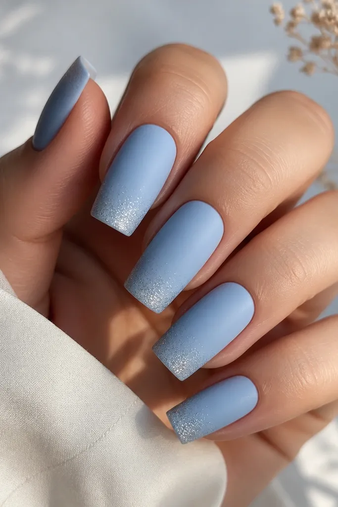 Glossy-to-matte contrast nails. The main color is matte powdery sky blue on all nails. At the tips, there's a faint gradient of tiny silver micro-glitter fading upward.
