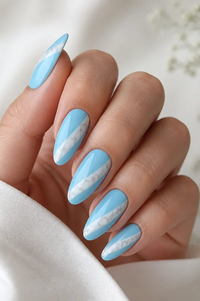 Almond nails with a glossy sky blue base. On each nail, a single white marble swipe runs diagonally from near the cuticle to the side of the tip, with thin gray veins.