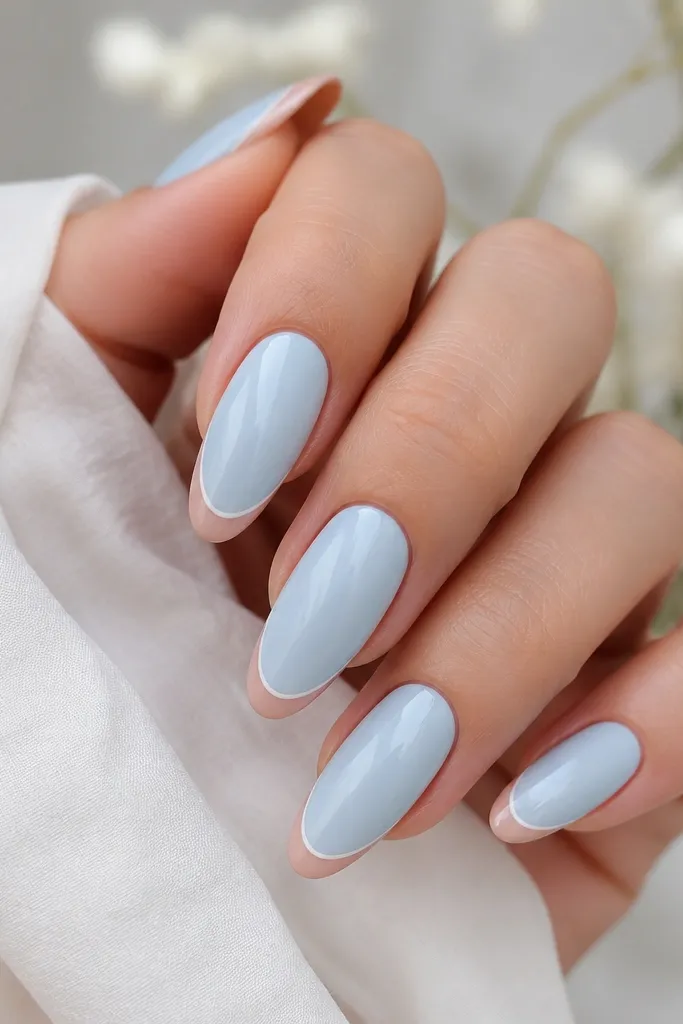Long oval nails. The nail has a sky blue background. At the tip, there is a nude reverse French band creating a clean arc, plus a thin white line on the arc.