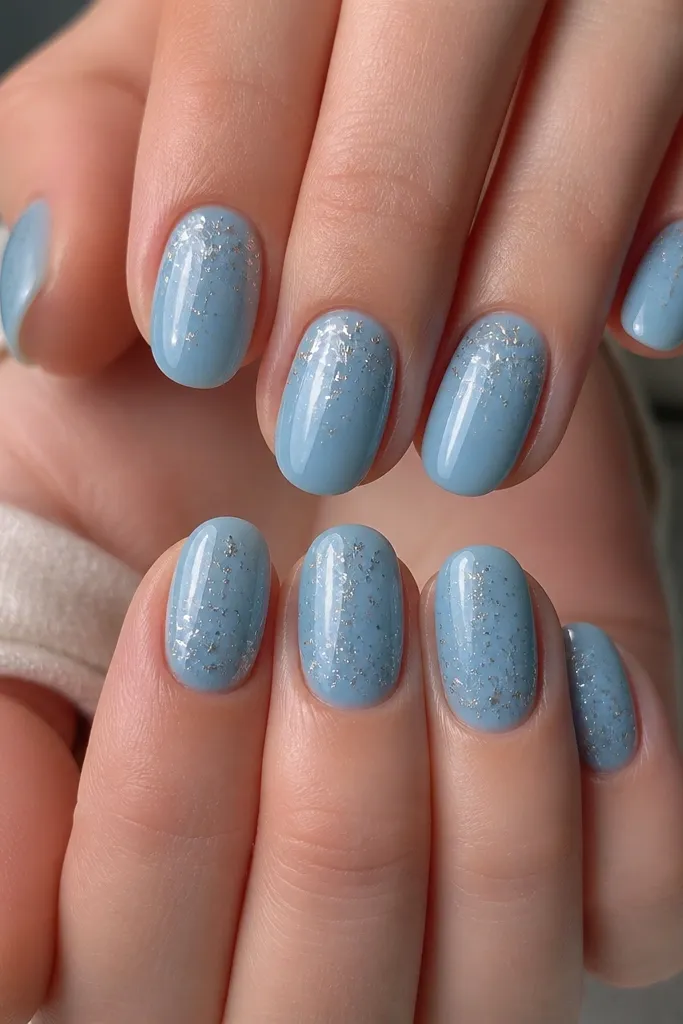 Glassy sky blue nails. Each nail has scattered tiny silver star-shaped flecks concentrated near the cuticle and fading toward the tip.