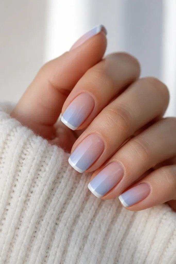 Ombre nails that start nude and fade into sky blue. Along the very free edge there's a thin white 'frost' strip, like a snow line.