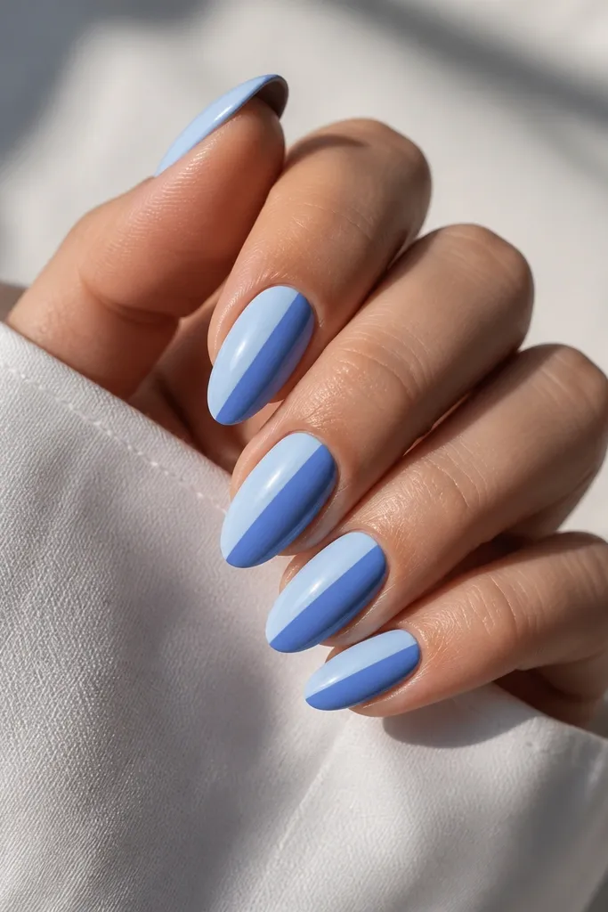 Medium almond nails with diagonal split panels. One side is pale sky blue, the other is deeper cornflower blue. The split line is crisp and slightly off-center.