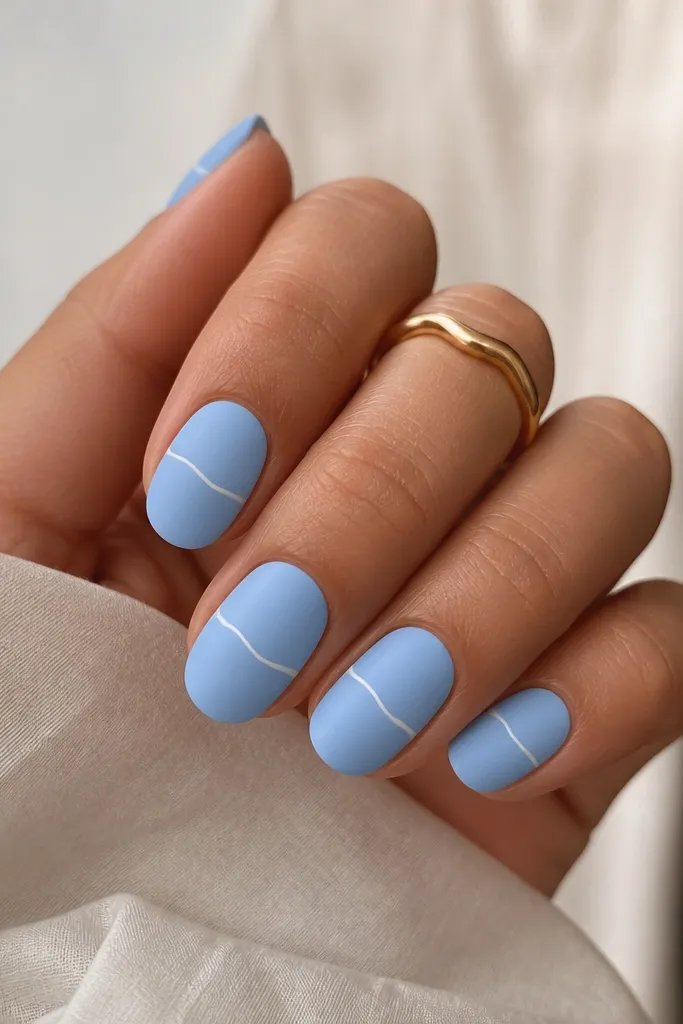 Powder blue nails are matte. A thin glossy white line curves horizontally like a waterline across the middle of each nail.