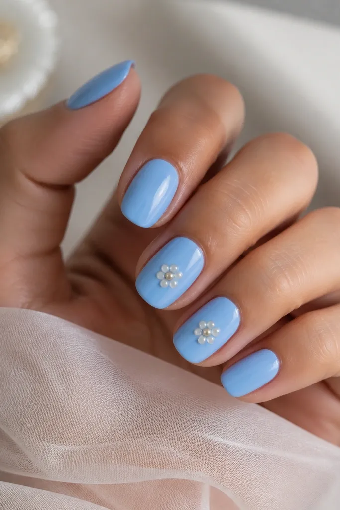 Nails are sky blue. On two nails, small flower shapes are made from white dots around a single tiny pearl bead at the center.