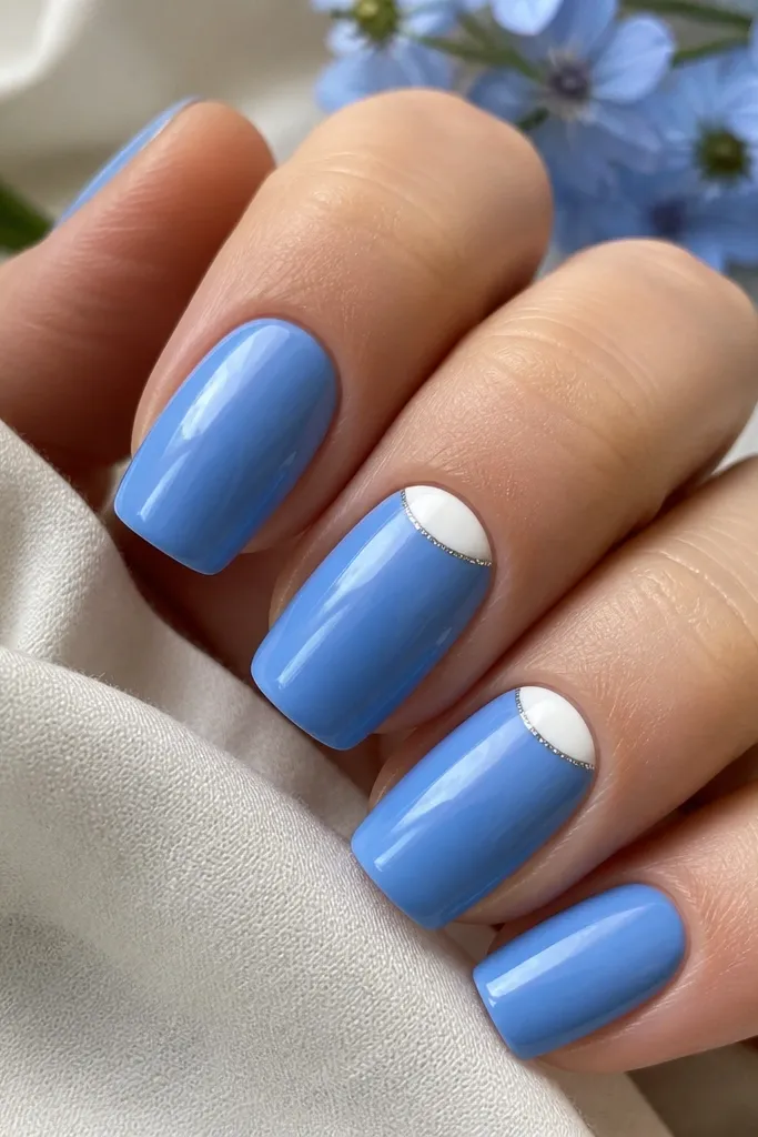 Four nails in sky cornflower blue with glossy finish; two accent nails show thin white half-moons at the base, each half-moon outlined with a fine silver line.