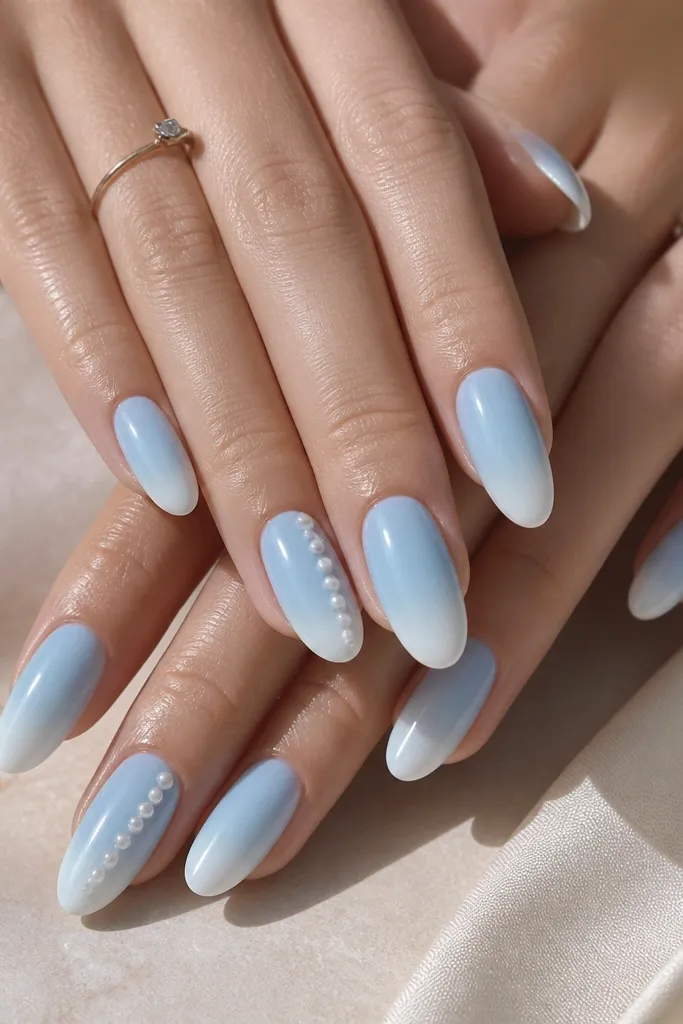 Powdery sky blue base with glossy finish; tips fade into a soft white at the edge; a few nails have tiny pearl 'drips' shaped like small beads down the center.