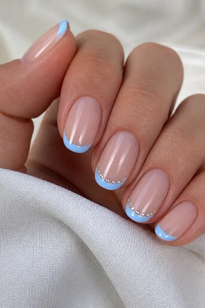 Clear nude base with sky blue micro French tips; along the smile line are tiny silver micro rhinestones spaced evenly on two nails.
