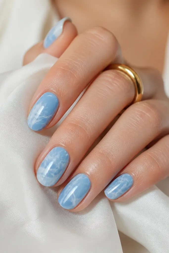 Sky blue marble swirls across nails with soft white veins; the base is glossy and the marble lines look thin like natural stone.