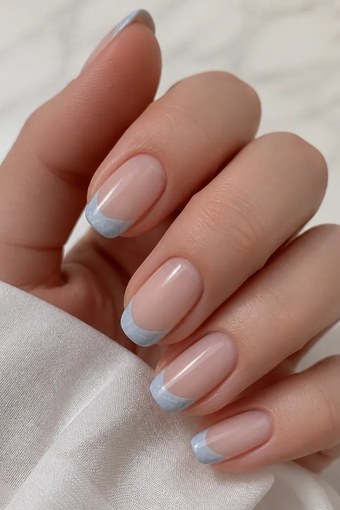 Nude base with icy sky blue French tip; the tip has thin white marble lines and a glossy finish.