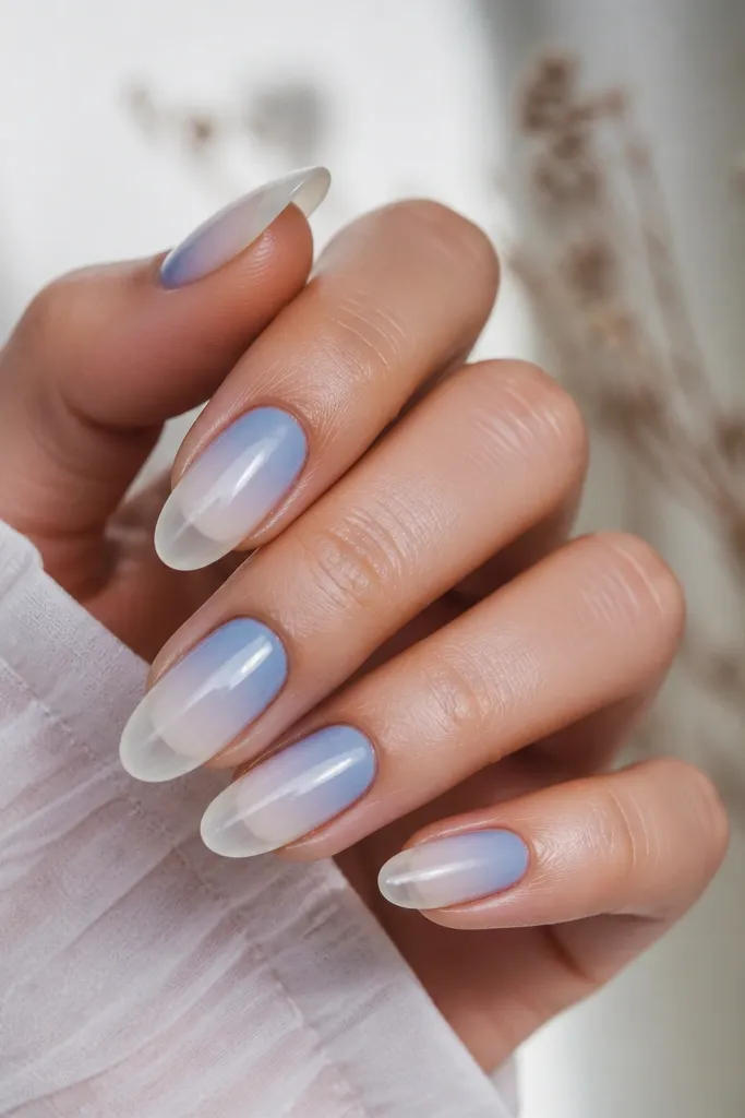 Nails show sky blue at the base that fades smoothly into a nearly clear tip. The gradient is soft, with no harsh line. Tips look glossy and glassy.