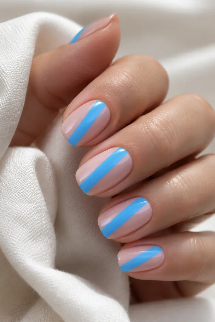 Each nail has a nude glossy base. One diagonal stripe runs from lower-left near the cuticle to upper-right toward the tip in bright sky blue. The stripe edges are razor straight.