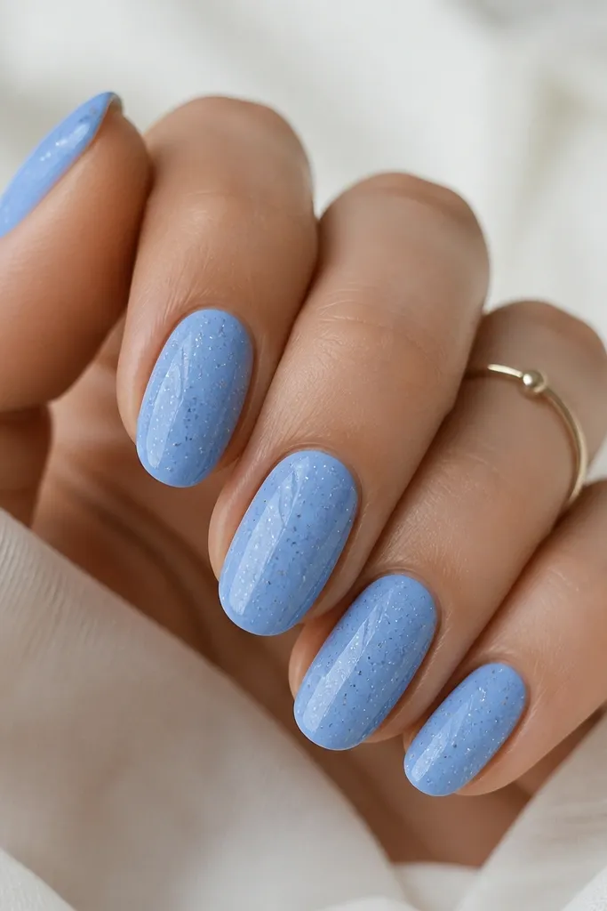 Sky blue nails with scattered tiny white and silver specks across the surface. The specks vary in size, like stars on a night sky.