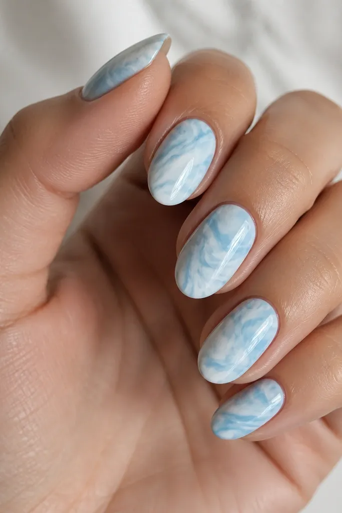 White and sky blue swirls run across the nails like marble. The pattern is organic, with thin lines and soft feathering. The overall finish is glossy.