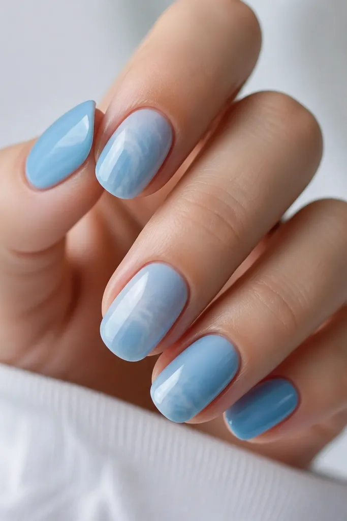 Mixed nails: some are sky blue solid, others show milk-bath marble. White veins curl through the blue like marbling in resin, with a glossy finish.