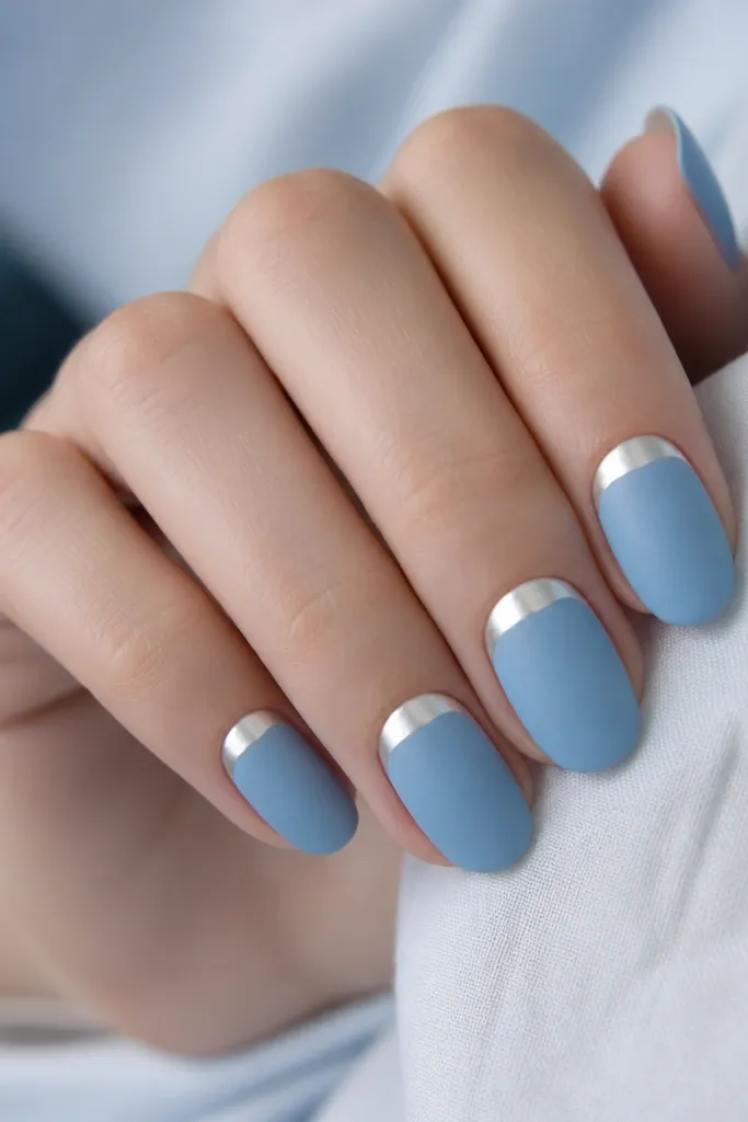 Nails are matte sky blue. Each nail has a glossy white or silver half-moon at the cuticle area, creating a crisp crescent shine.