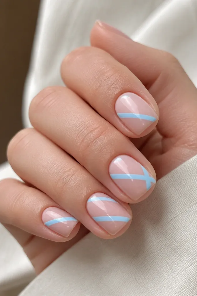 Short nails on a nude-pink base with two diagonal sky blue stripes crossing near the center. The stripes are straight, glossy, and separated by negative space.