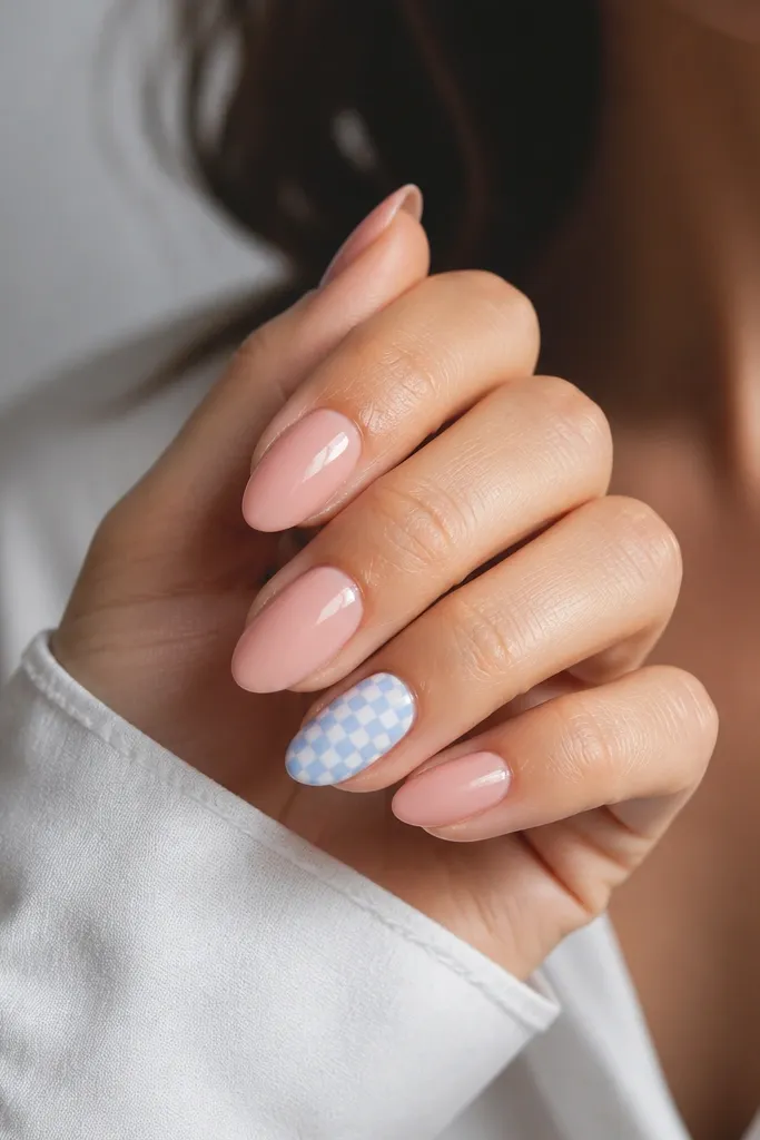 Nude-pink nails with one accent nail showing a mini sky blue checkerboard pattern. The checker squares are tiny and crisp with glossy finish.