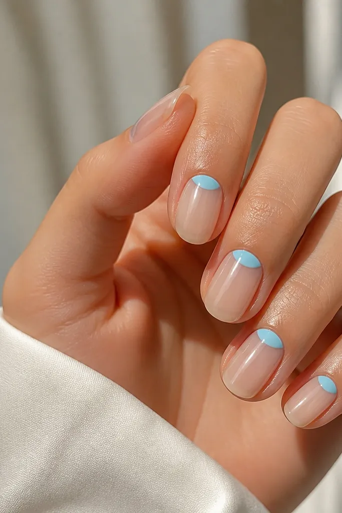 A clear-to-nude base with a sky blue half-moon at the cuticle on each nail, with the rest of the nail left sheer and glossy.