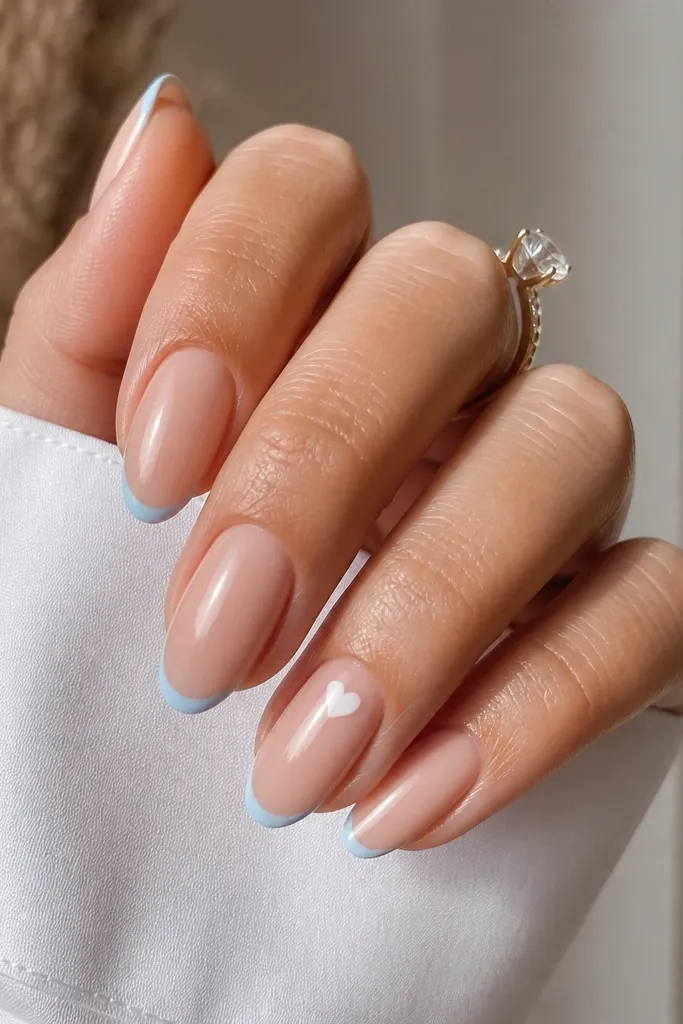 Soft nude base with a very thin sky blue French line at the tips and a tiny white heart on one accent nail near the cuticle line, glossy finish.