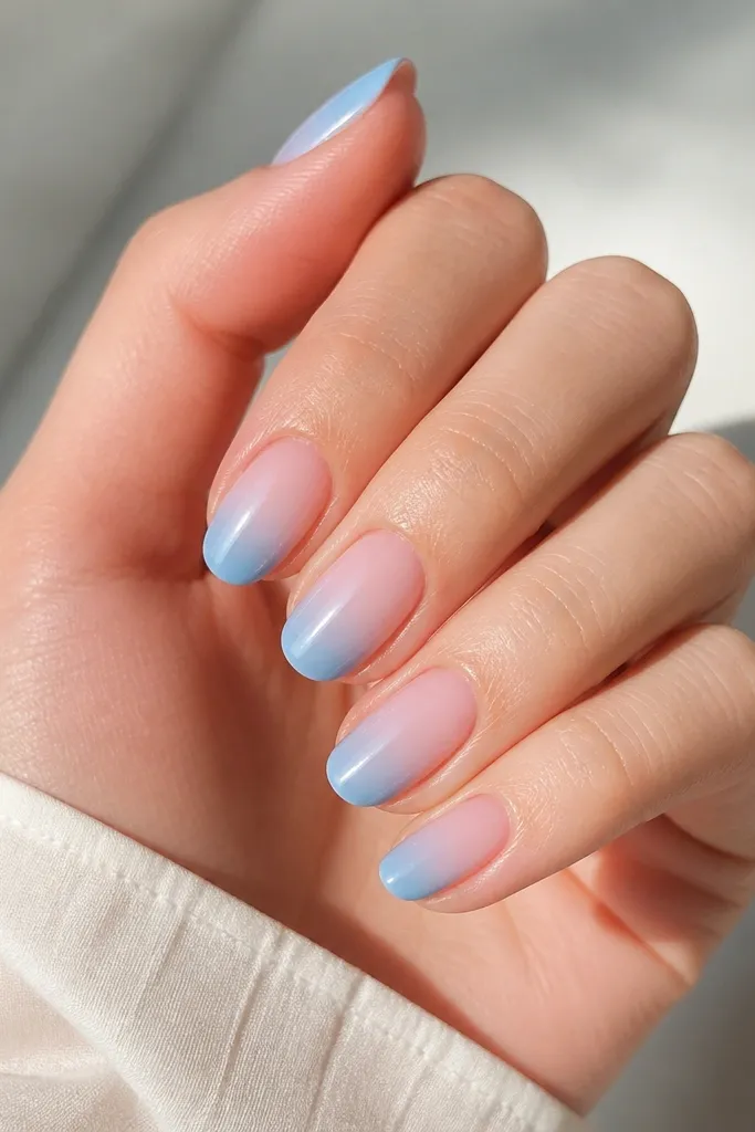 Nails with sky blue fading from the tips toward a clearer center, like an ombre, glossy finish.
