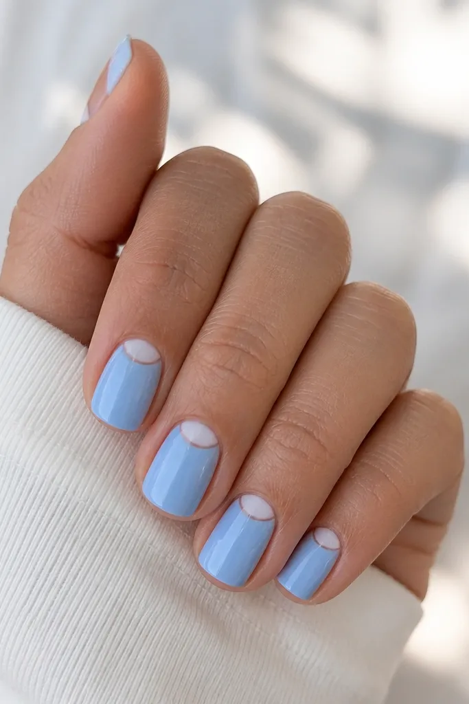 Short nails in powder sky blue with a tiny white half-moon near the cuticle on each nail. The rest of the nail is solid blue, and the finish is glossy.