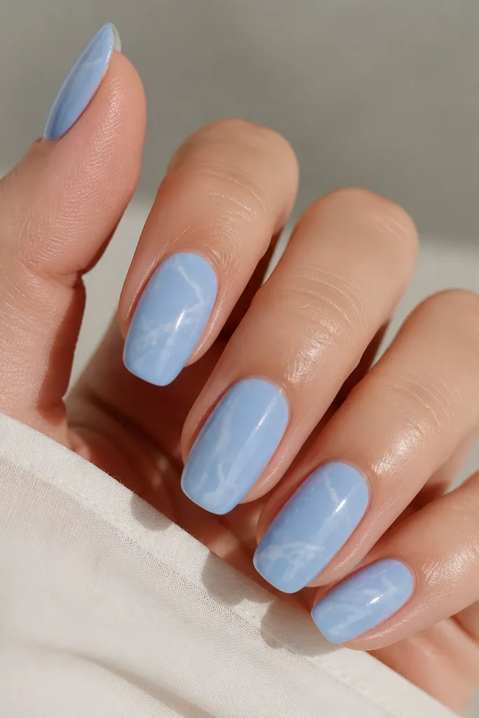 Sky blue nails with soft white marbling lines that look like thin marble veins; the marbling varies slightly across nails and stays glossy.